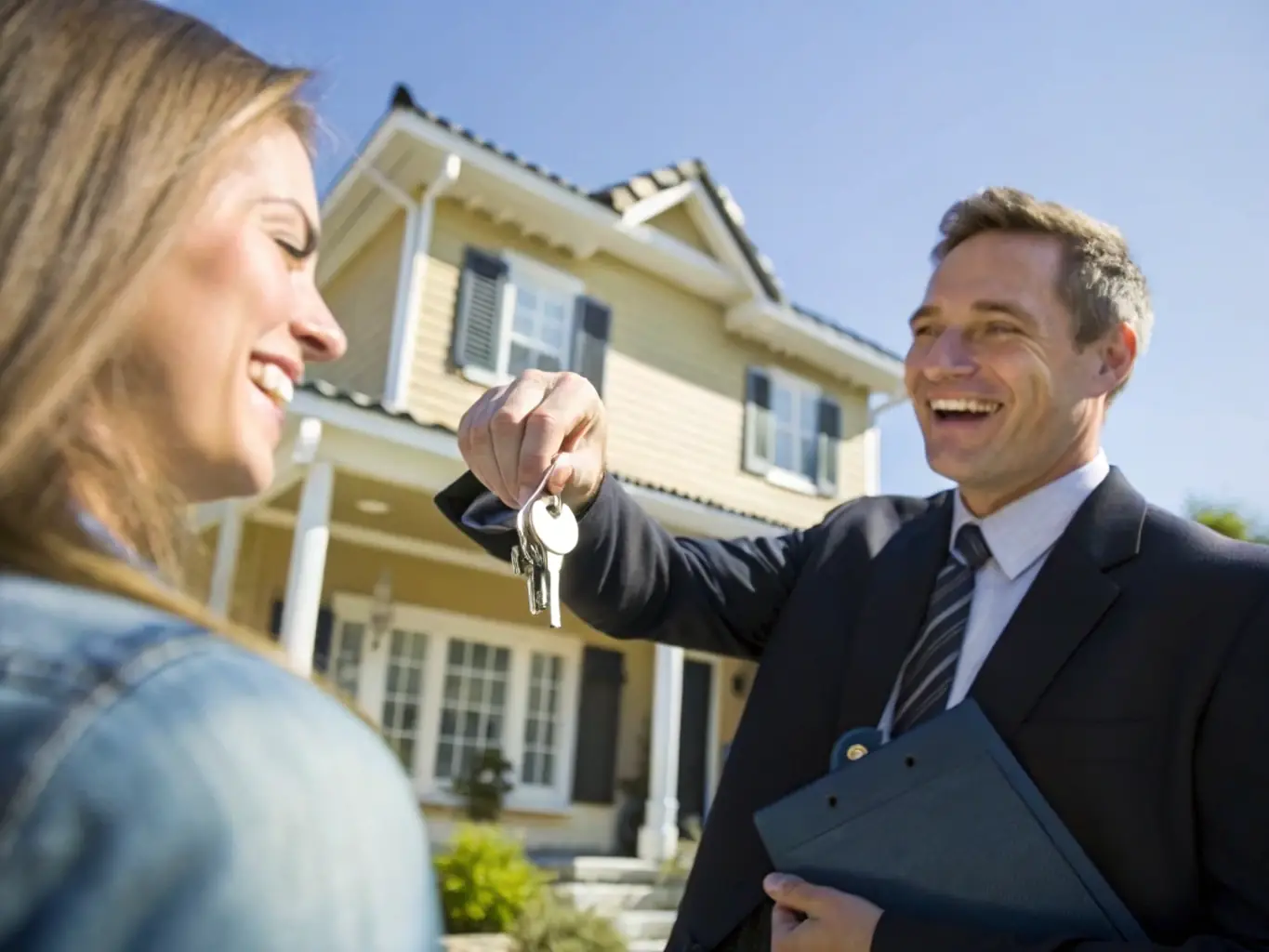 A professional photograph of a real estate agent handing over keys to a smiling client in front of a modern apartment building in Dubai, representing property selling services.